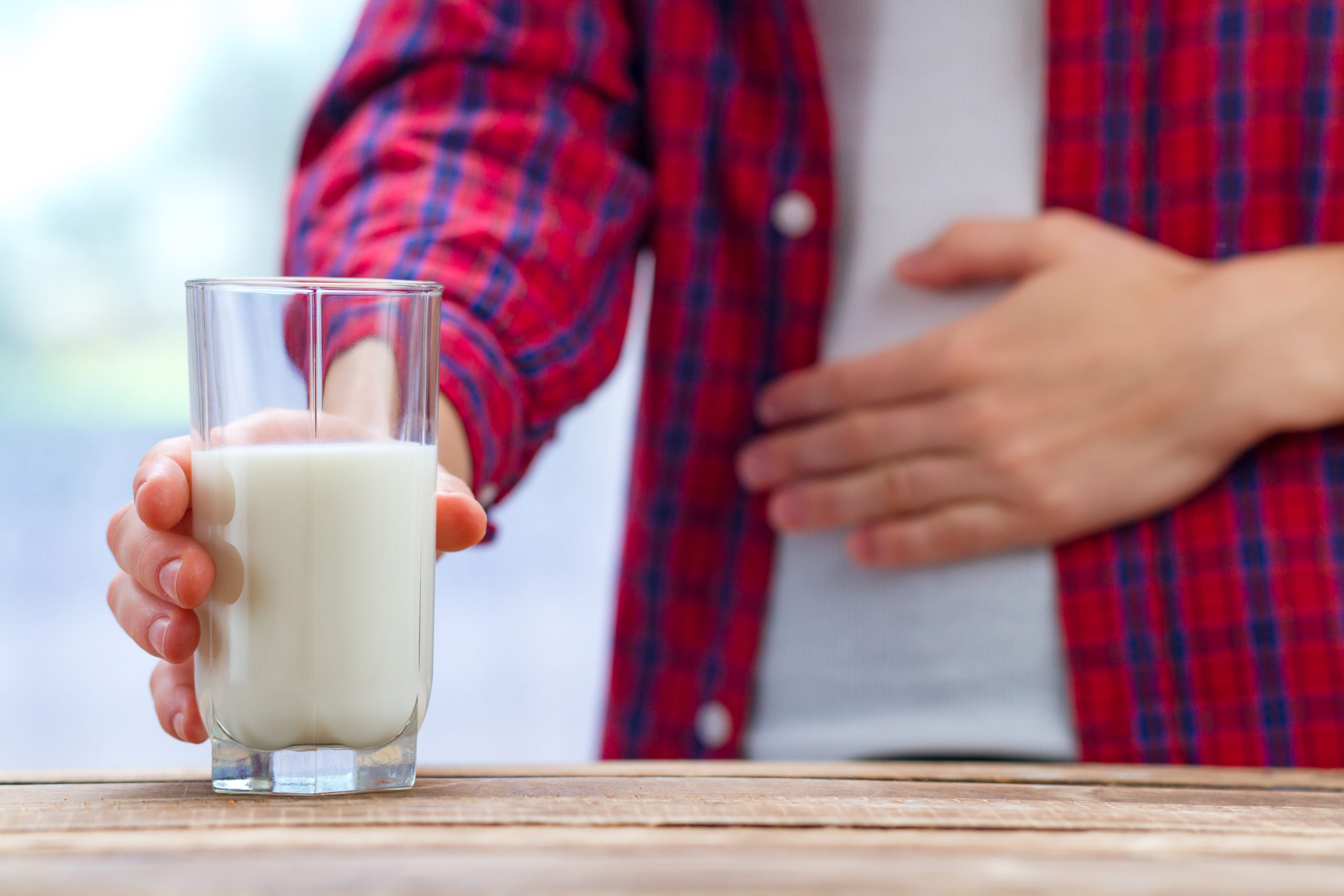 Image of a man holding a glass of milk with one hand and his stomach with the other